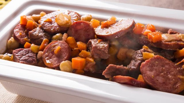 South American cuisine: Puchero soup with sausage. close-up in a pot on the table with smoke.