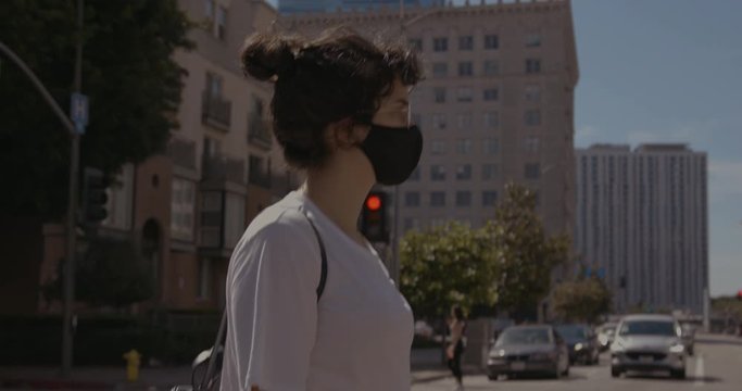 Woman Wearing a Face Mask Crosses Street Left to Right in Downtown Los Angeles Intersection During Corona Virus Pandemic