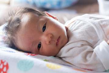 The adorable cute newborn baby infant with big black eyes lying on the bed and smilling