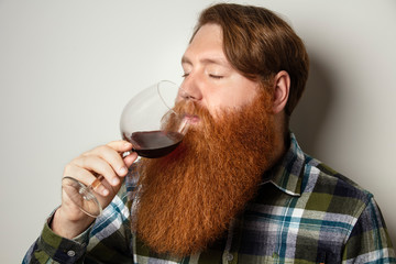 A red-bearded man drinking wine from a large glass. A vine tasting at home. Sommelier for yourself at home. A man with a big beautiful beard.