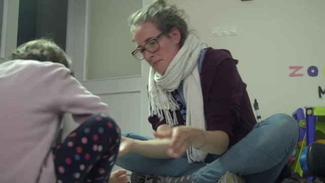 Young Caucasian mother mixes white paint and paints child's foot, close up