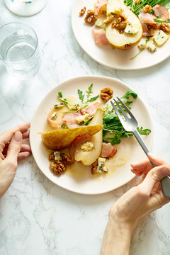 Female hands holding a plate of pear salad with walnuts, prosciutto, arugula and blue cheese. Dinner appetizer on marble table
