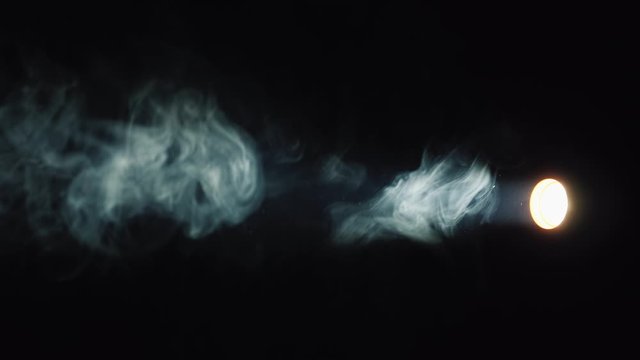 A flashlight beam illuminates the smoke on a black background