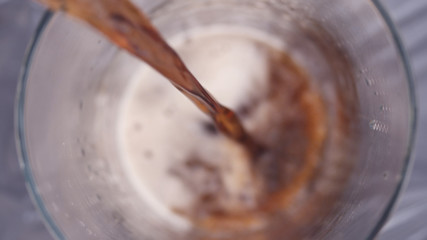 Close up of Dark Beverage being Poured into Glass Cup. Foam and Bubbles Raise as the Glass is Filled with Straight Stream of Fizzy Liquid.