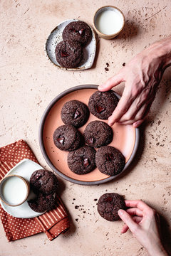 Hands selecting double chocolate ginger cookies from a plate.