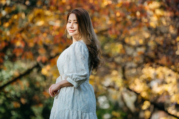 Beautiful asian woman with autumn leaves, flower and fall yellow leaves background at Hagley park, Christchruch, New Zealand.