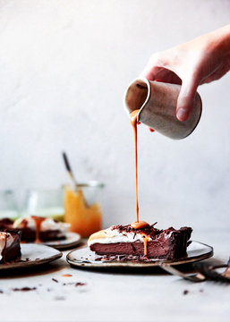Woman's hand pouring caramel on slice of chocolate tart