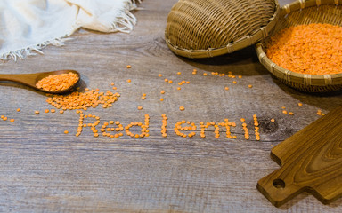 Word "red lentils" in English on wooden background. Bamboo basket, spoon and white cloth on the corner.