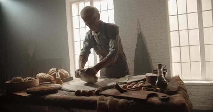Experienced moustached senior caucasian baker kneading dough for his traditional recipe. Mature man enjoying his new hobby after retirement, making homemade bread 4k footage
