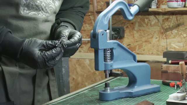 Close up of man tanner in black gloves uses a press to install metal fittings. Working process in the leather workshop.