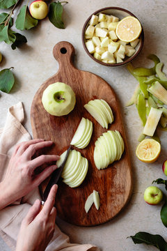 Hand held knife slicing apples on a wooden cutting board.