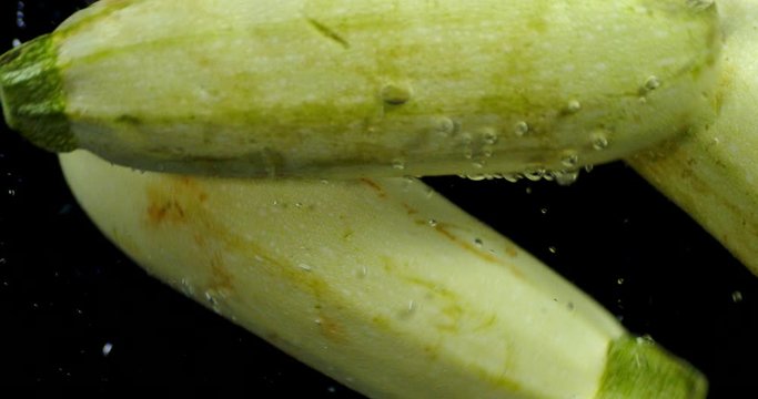 Whole zucchini fall under water with air bubbles.