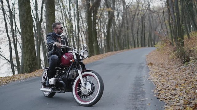 Pretty blonde comes to her smiling biker sitting at motorcycle in park