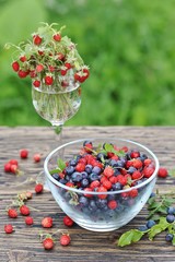 berries of wild strawberries and forest blueberries on a background of nature on an old rustic board. Country style. Soft focus. Space for text