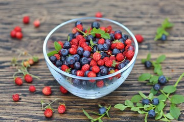 berries of wild strawberries and forest blueberries on a background of nature on an old rustic board. Country style. Soft focus. Space for text