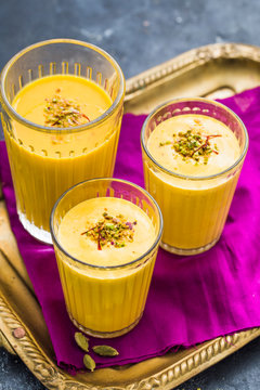 Three glasses of Mango Lassi garnished with saffron and crushed pistachio