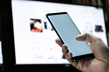 Mock up mobile phone in hand with monitor background. Concept for mobile application technology and online e-commerce.