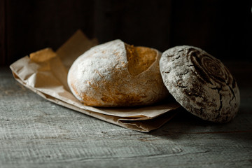 Healthy rye whole grain round bread on brown craft paper on black wooden table. Home baked