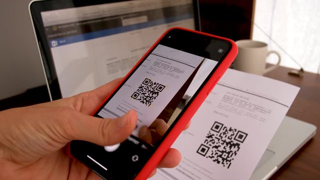 Hand with phone scans QR Code on background of a laptop with a workplace