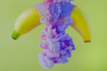 A banana fruit with partial focus of dissolving pink and purple poster color in water on yellow...