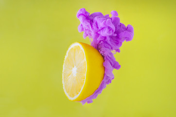 Slice lemon with partial focus of dissolving violet poster color in water on yellow background for summer, abstract and background concept.