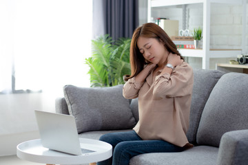Tired Asian woman feels neck pain after working on a computer for a long time and sitting in the...