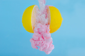 Partial focus of dissolving pink poster color in water drop between two slice lemons on blue...