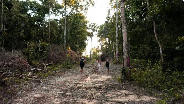 Three young people walking through a hidden jungle path to tropical Lazy Beach Cambodia, aerial
