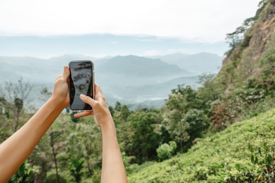 Closeup of  women hands holding mobile phone with wide touchscreen and making photos and video of beautiful nature landscape from high altitude in mountains. Low cloudy sky. Travel and discover