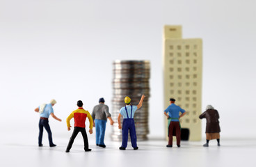 A variety of miniature people gathered in front of miniature buildings and piles of coins.
