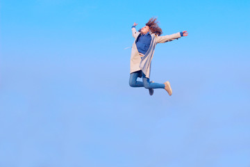 Fototapeta na wymiar Blurry image of a happy teenage girl jumping up, blue sky background, horizontal view. People, freedom, teens, travel concept.