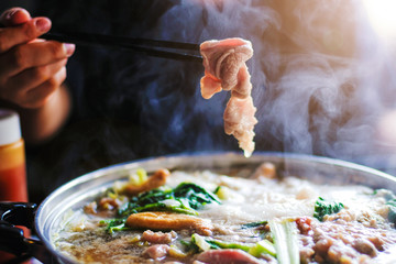Woman holding sliced beef meat by chopsticks shabu shabu is Korean or Japanese style beef in hot...