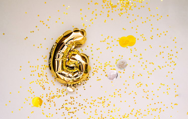 small foil gold balloons numbers 6 inflated with helium on a beige delicate background with gold sequins stars and balls. glittering holiday greeting layout