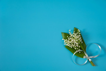 Flower composition. A bouquet of flowers and leaves of the may Lily of the valley (Convallaria majalis) with a gray bow on a light blue background. Free space.  Flat lay.