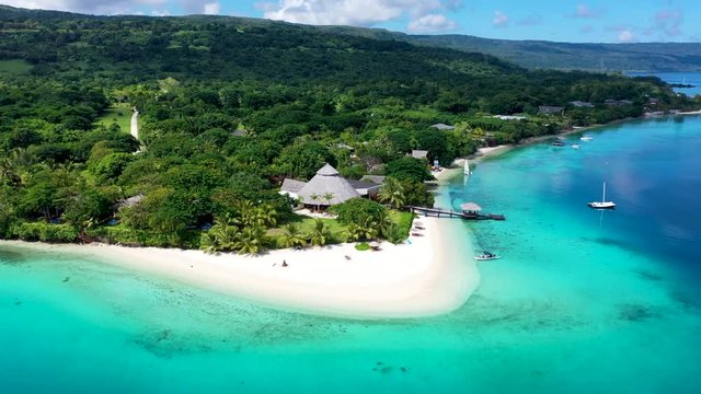 Vanuatu island resort with gorgeous turquoise water and boat beaching on white sand, circle aerial