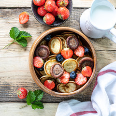 Tiny pancake cereal and chocolate mini pancakes in a wooden bowl with honey and strawberries on a wooden background. Top view. Copy space. Trendy food