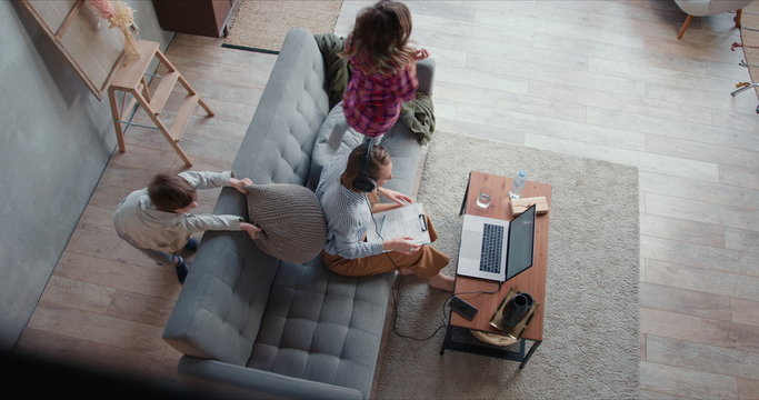 Top View Two Teenage Children Drive Their Young Mother Crazy While She Tries To Work From Home Online Using Laptop.