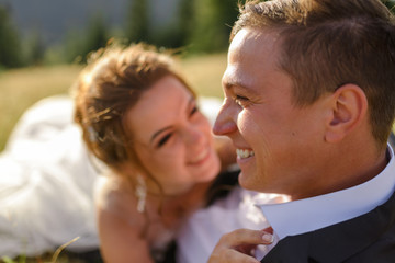 Fototapeta premium Wedding photography in the mountains. Newlyweds are lying in the grass. The couple is smiling. Close-up.