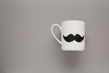 Happy fathers day, boss day concept, white tea or coffee mug with mustache on grey background, copy...