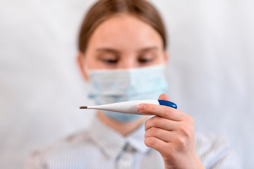 teenager girl, in medical mask, focus on thermometer electronic in hand, checking temperature, carefully virus disease and influenza, chills and illness, stay home, stop pandemic coronovirus covid 19