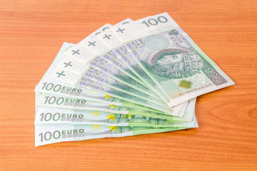 Fototapeta na wymiar 100 EUR and 100 PLN banknotes on wooden table.