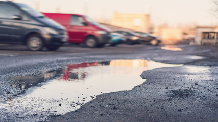 puddle in pit on destroyed asphalt road against blurry cars at spring sunset © Bonsales