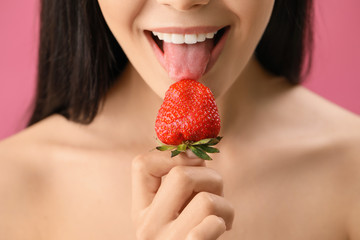 Sexy young woman with strawberry on color background, closeup