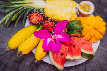 Colorful tropical fruits on big plate. On rustic wooden background. Top view