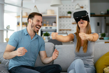 Smiling young woman using VR headset at home on couch. Woman and her husband enjoying virtual reality at her apartment.