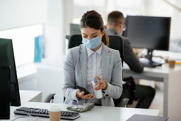 Businesswoman disinfecting her smart phone in the office.	