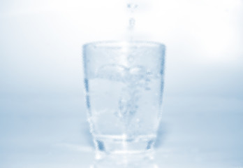 blurred glass bright water dripping into the glass with many bubble in water bright blue background . healthcare drinking advertising concept 