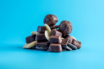 Pile of appetizing and tasty sweets on a blue background. Chocolates, white chocolate and cookies. Concept of unhealthy food and the harm of sugar