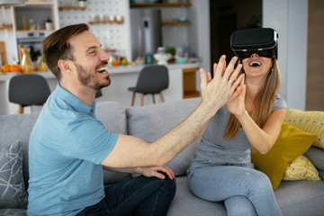 Smiling young woman using VR headset at home on couch. Woman and her husband enjoying virtual reality at her apartment.