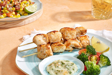 Grilled chicken skewers dish on light orange background, served with mayonnaise sauce. Front View